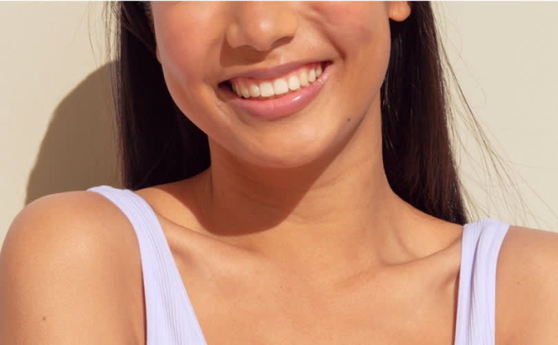 A close-up shot of a young woman in a purple shirt, smiling with healthy-looking teeth