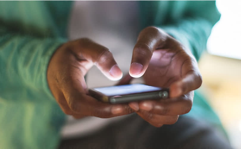 A man in a green sweater typing into his smartphone 